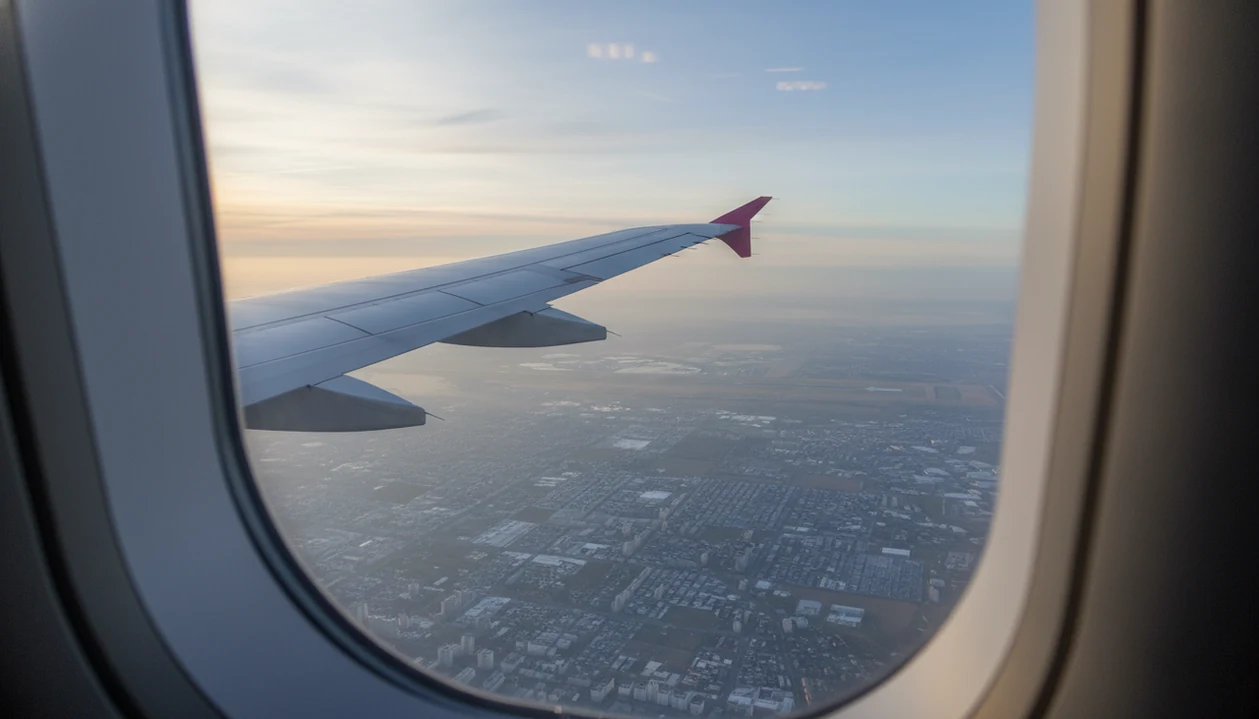 An airplane wing seen through a window during a calm descent toward the ground below.